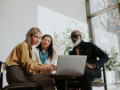 diverse group of three people - two women and an older man with beard - working at a laptop